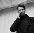 Fashion beard style business handsome male model in style clothing blue jacket and speaking on mobile phone on street wall Royalty Free Stock Photo