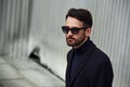 Fashion beard style business handsome male model in fashion sunglasses and blue coat with serious concentrated look posing in Royalty Free Stock Photo