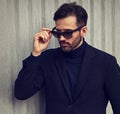 Fashion beard style business handsome male model in fashion sunglasses and blue coat with serious concentrated look posing in Royalty Free Stock Photo