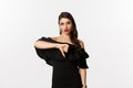 Fashion and beauty. Disappointed sassy woman in black dress, showing thumbs down, dislike something bad, judging over Royalty Free Stock Photo