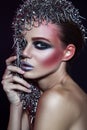 Fashion beauty model with metallic headwear and shiny silver red makeup and blue eyes and red eyebrows on black background Royalty Free Stock Photo