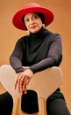 Fashion, beauty and muslim woman on chair with stylish hat, cosmetics and trendy makeup on studio background. Mature