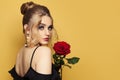 Fashion beauty portrait of beautiful woman with blonde hairdo and makeup holds red rose flower on black background Royalty Free Stock Photo