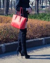 Fashion blogger girl posing in the street in a black suit trending, high-heeled boots and a big red hand bag Royalty Free Stock Photo