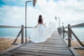 Fashion bride walking down pier on the beach in a white dress. Beautiful girl walks barefoot down the beach. Royalty Free Stock Photo
