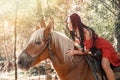 Fashion. A brunette woman in a red dress sits astride a brown horse. Summer, sunlight