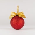 Fashion christmas background in simple minimal style - bright glitter red ball with golden bow stand on white table with soft. Royalty Free Stock Photo