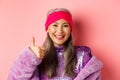 Fashion. Close-up of asian old lady in stylish disco outfit showing thumb-up, approve and like something, smiling Royalty Free Stock Photo