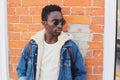 Fashion close-up portrait african man wearing jeans jacket, black sunglasses on city street over brick wall