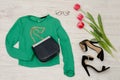 Fashion concept. Green blouse, handbag, sunglasses, black shoes and pink tulips. Top view, light wood background Royalty Free Stock Photo