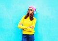 Fashion cool girl in headphones listening to music wearing colorful pink hat yellow sunglasses sweater over blue background Royalty Free Stock Photo