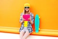 Fashion cool girl using tablet pc in city with skateboard over colorful orange Royalty Free Stock Photo