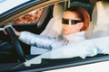 Fashion cyberpunk girl drive a supercar. Red hair woman with futuristic eyeglasses sits by the car steering wheel