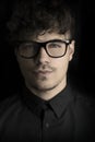 Fashion dark portrait of young man with glasses on black background. Portrait of intelligent man. Photo portrait curly guy