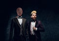 A fashion designer with expressive style posing next to a mannequin in exclusive custom made men`s suit in a dark tailor Royalty Free Stock Photo