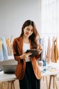 Fashion designer woman talking smart phone and using laptop with digital tablet computer in modern studio the clothes hanging on Royalty Free Stock Photo