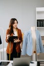 Fashion designer woman talking smart phone and using laptop with digital tablet computer in modern studio the clothes hanging on Royalty Free Stock Photo