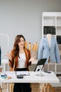 Fashion designer woman talking smart phone and using laptop with digital tablet computer in modern studio the clothes hanging on Royalty Free Stock Photo