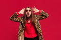 Fashion diva. Portrait of young man with long hair posing in stylish fur coat and sunglasses against red studio