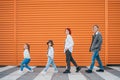 Fashion-dressed quartet of small kids and teenagers sisters and brothers crossing a pedestrian zebra crosswalk on the orange wall