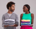 Fashion faceoff. Studio shot of a young man and woman each holding a neatly folded pile of clothes.