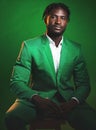 Fashion, formal and black man in a green suit sitting on a chair in studio with a luxury outfit. Elegant, stylish and Royalty Free Stock Photo