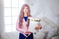 Fashion freak. Glamour synthetic girl, fake doll with empty look and long lilac hair is holding box with flowers while