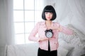 Fashion freak. Glamour synthetic girl, fake doll with empty look and short black hair is holding clock while standing in