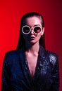 Fashion girl with long hair and round sunglasses in a black shining dress poses in neon light in the studio