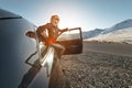 Fashion girl standing next to a retro sports car in the sun. Stylish woman in a leather suit is waiting near a classic Royalty Free Stock Photo