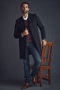 Fashion goals. Studio portrait of a stylishly dressed young man standing next to a chair against a gray background. Royalty Free Stock Photo