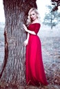 Fashion gorgeous young blonde woman in beautiful red dress in a fairy-tale forest. magic atmosphere. Retouched toning shot Royalty Free Stock Photo