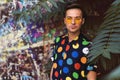 Fashion guy in retro glasses stands under a palm tree against the background of a graffiti wall in retro clothes Royalty Free Stock Photo