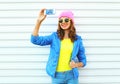 Fashion happy cool smiling girl in colorful clothes taking picture makes self portrait on smartphone over white background Royalty Free Stock Photo