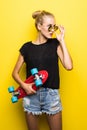 Fashion happy smiling hipster cool girl in sunglasses with skateboard having fun outdoors against the yellow background Royalty Free Stock Photo