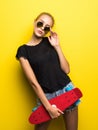 Fashion happy smiling hipster cool girl in sunglasses with skateboard having fun outdoors against the yellow background Royalty Free Stock Photo