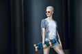 Fashion happy smiling hipster cool girl in sunglasses with skateboard behind the black urban background. Royalty Free Stock Photo