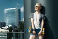 Fashion happy smiling hipster cool girl in sunglasses with skateboard behind the city urban outdoor background. Royalty Free Stock Photo