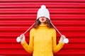 Fashion happy woman blowing red lips makes air kiss wearing colorful knitted hat, yellow sweater over red