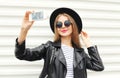 Fashion happy woman makes self portrait on smartphone in black rock style over city white Royalty Free Stock Photo