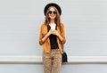 Fashion happy young smiling woman with coffee cup wearing retro elegant hat, sunglasses, brown jacket and black handbag Royalty Free Stock Photo