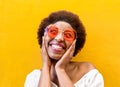 Fashion hippie african woman smiling and wearing sunglasses with yellow ochre wall in background - Black afro girl having fun - Royalty Free Stock Photo