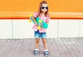 Fashion kid - stylish little girl child with skateboard wearing sunglasses in city Royalty Free Stock Photo