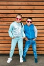 Fashion kids in the city stands on a wooden wall. Trendy boy and girl in sunglasses standing on the street Royalty Free Stock Photo