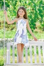 Fashion kids dress. Happy little child girl on a swing in the summer park. Happy kid having fun outdoors. Royalty Free Stock Photo