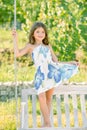 Fashion kids dress. Little child girl is swinging on a swing in summer park. Sunny joyful summer day. Child girl having Royalty Free Stock Photo