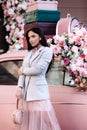 Fashion lady model in pink jacket skirt, makeup and black hair over retro car decorated with roses Royalty Free Stock Photo