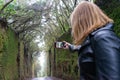 Fashion Lady touch the lcd screen of the phone to make and snapshot of the moss in the wall of the experience in the rainforest.