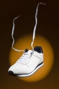 Fashion and Lifestyle Concepts. One New White Sneaker With Flying Shoelaces Placed Over Yellow Background With Circular Spotlight