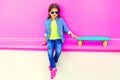 Fashion little girl child sitting with skateboard in city on colorful pink wall